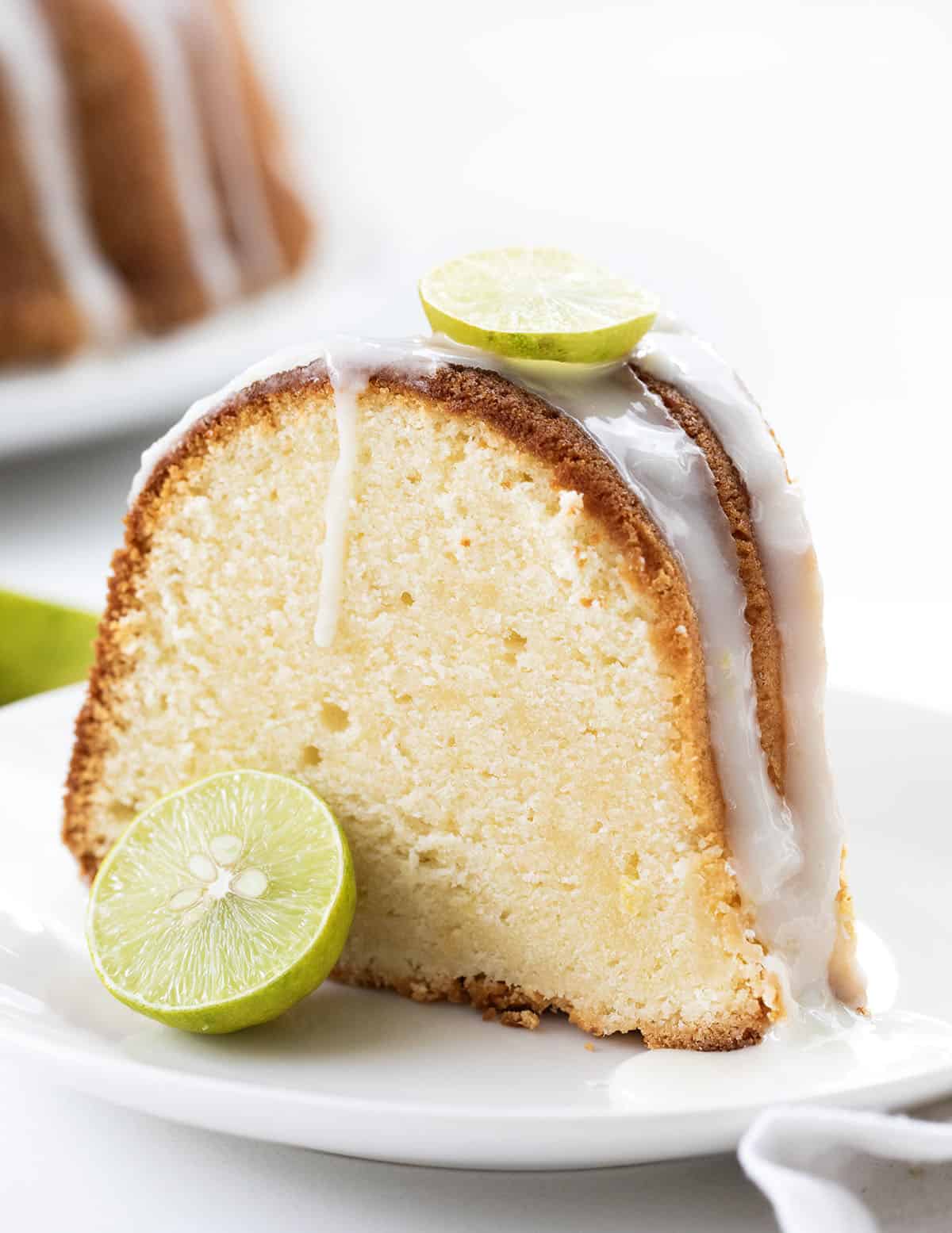 Slice of Key Lime Pound Cake on a white table in front of the rest of the cake Slice of Key Lime Pound Cake on a white table in front of the rest of the cake.