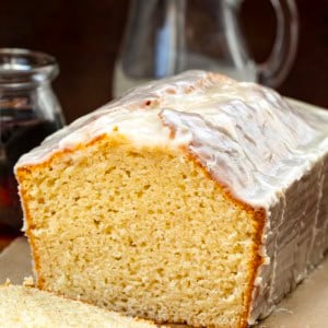Cut into loaf of Maple Glazed Donut Bread on a wooden table with maple syrup and glaze.