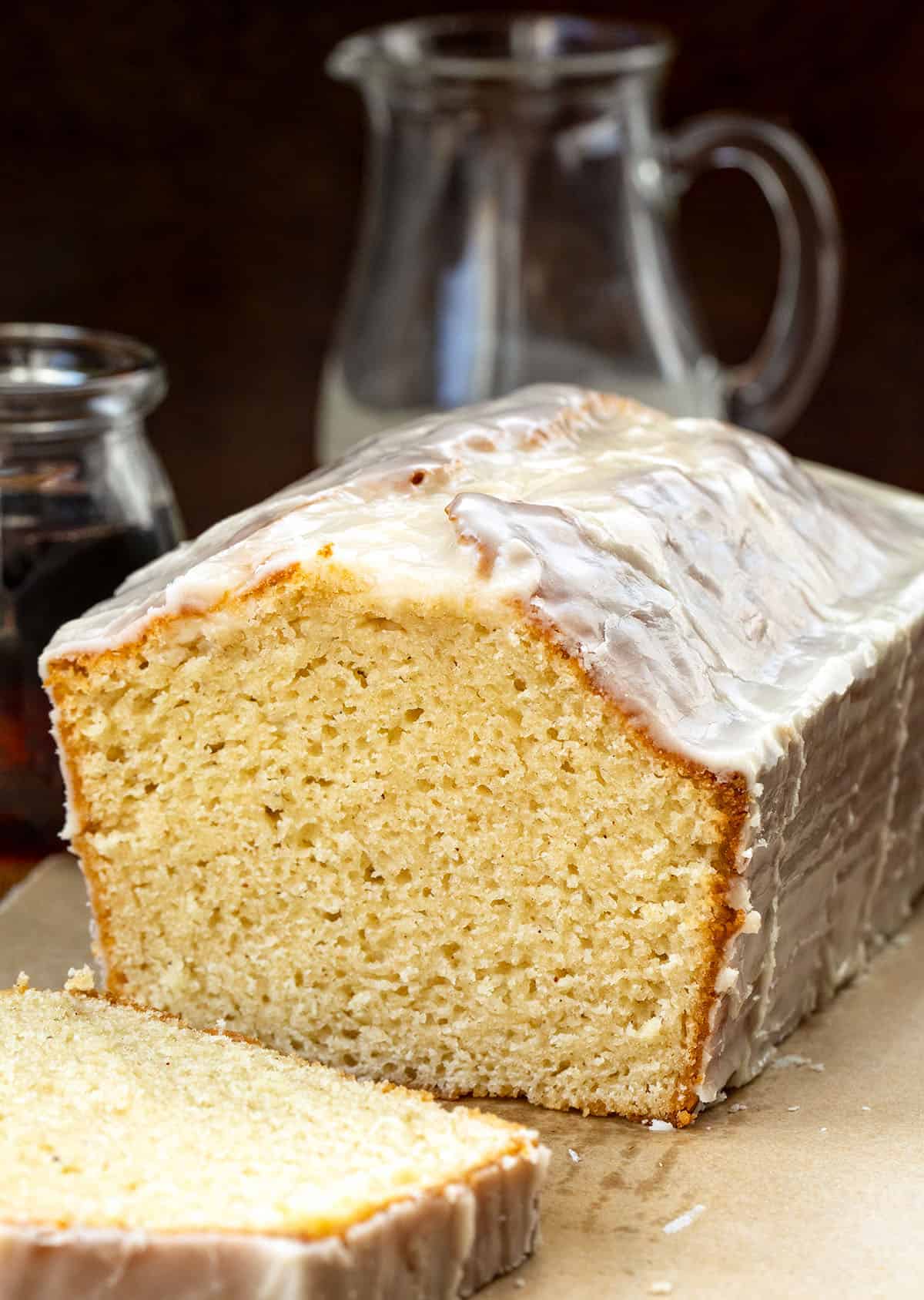 Cut into loaf of Maple Glazed Donut Bread on a wooden table with maple syrup and glaze.