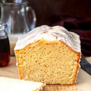 Cut into loaf of Maple Glazed Donut Bread on a wooden table with maple syrup and glaze.