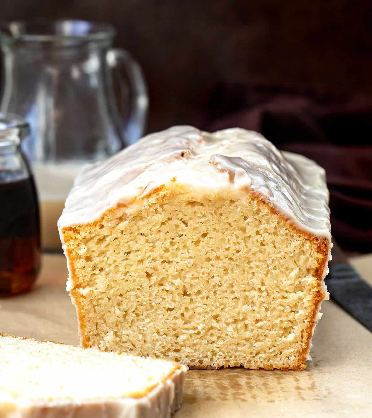 Cut into loaf of Maple Glazed Donut Bread on a wooden table with maple syrup and glaze.