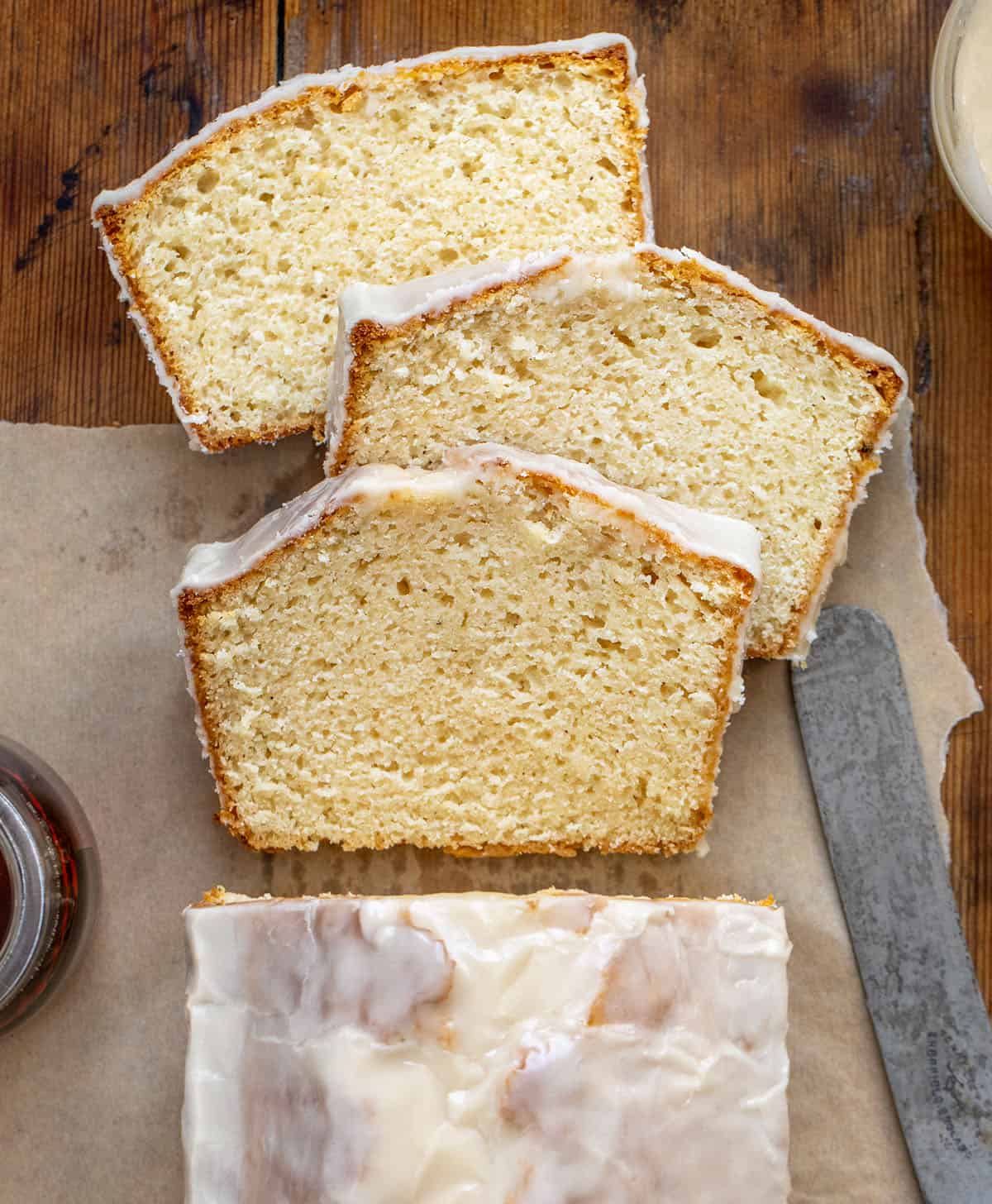 Slices of Maple Glazed Donut Bread cut and laying flat near the loaf on a wooden table from overhead.