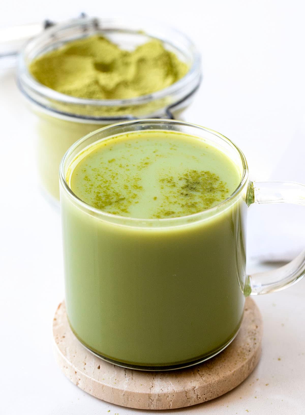 Hot Matcha Latte in front of a container of Matcha Latte Mix Hot Matcha Latte in front of a container of Matcha Latte Mix.
