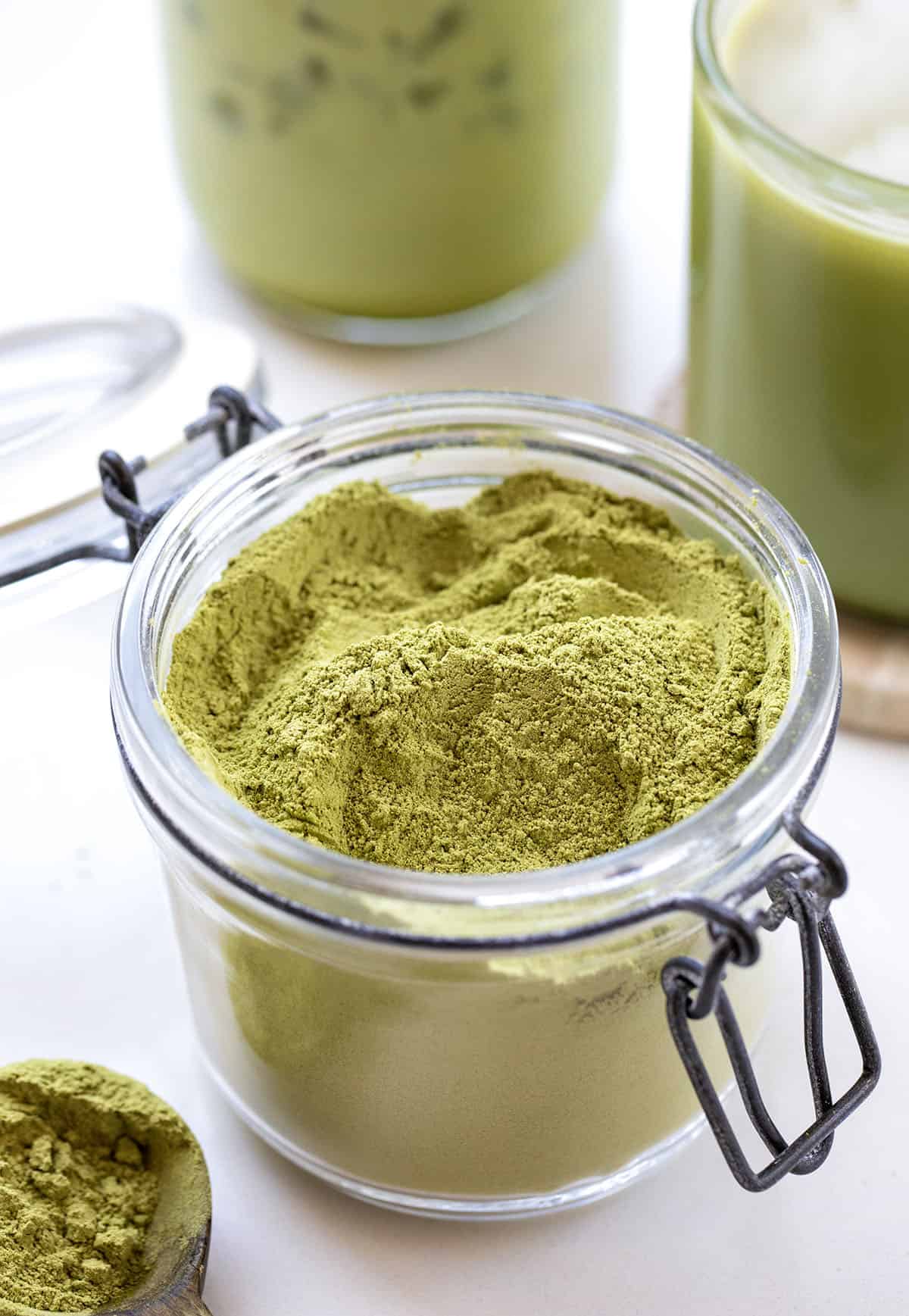 Matcha Latte Mix in front of an Iced Matcha Latte and a hot Matcha Latte on a white table.