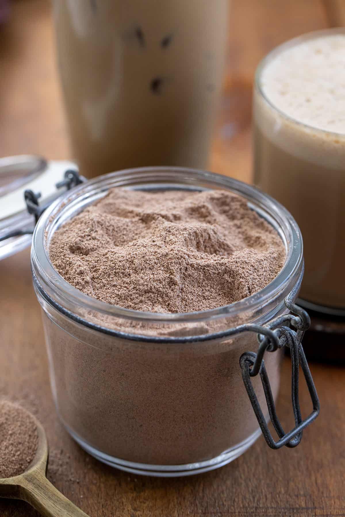 Jar of Mocha Latte Mix with an iced mocha latte and a hot mocha latte prepared int he background Jar of Mocha Latte Mix with an iced mocha latte and a hot mocha latte prepared int he background.