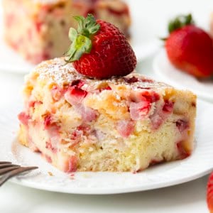 Slice of Old Fashioned Strawberry Sheet Cake on a white plate with a bite removed and fork resting on the plate.