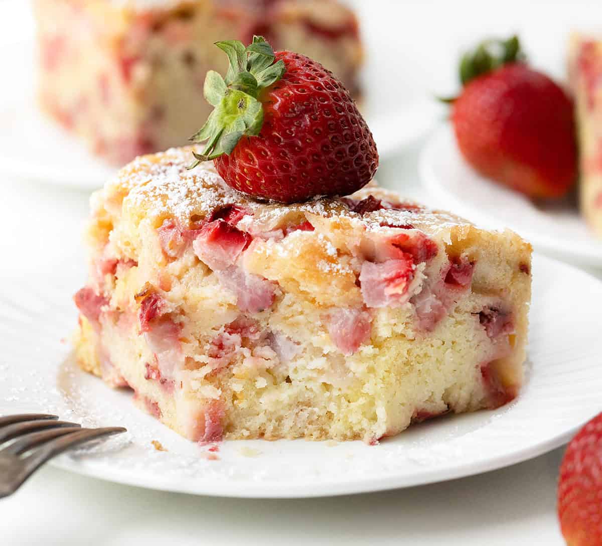 Slice of Old Fashioned Strawberry Sheet Cake on a white plate with a bite removed and fork resting on the plate.