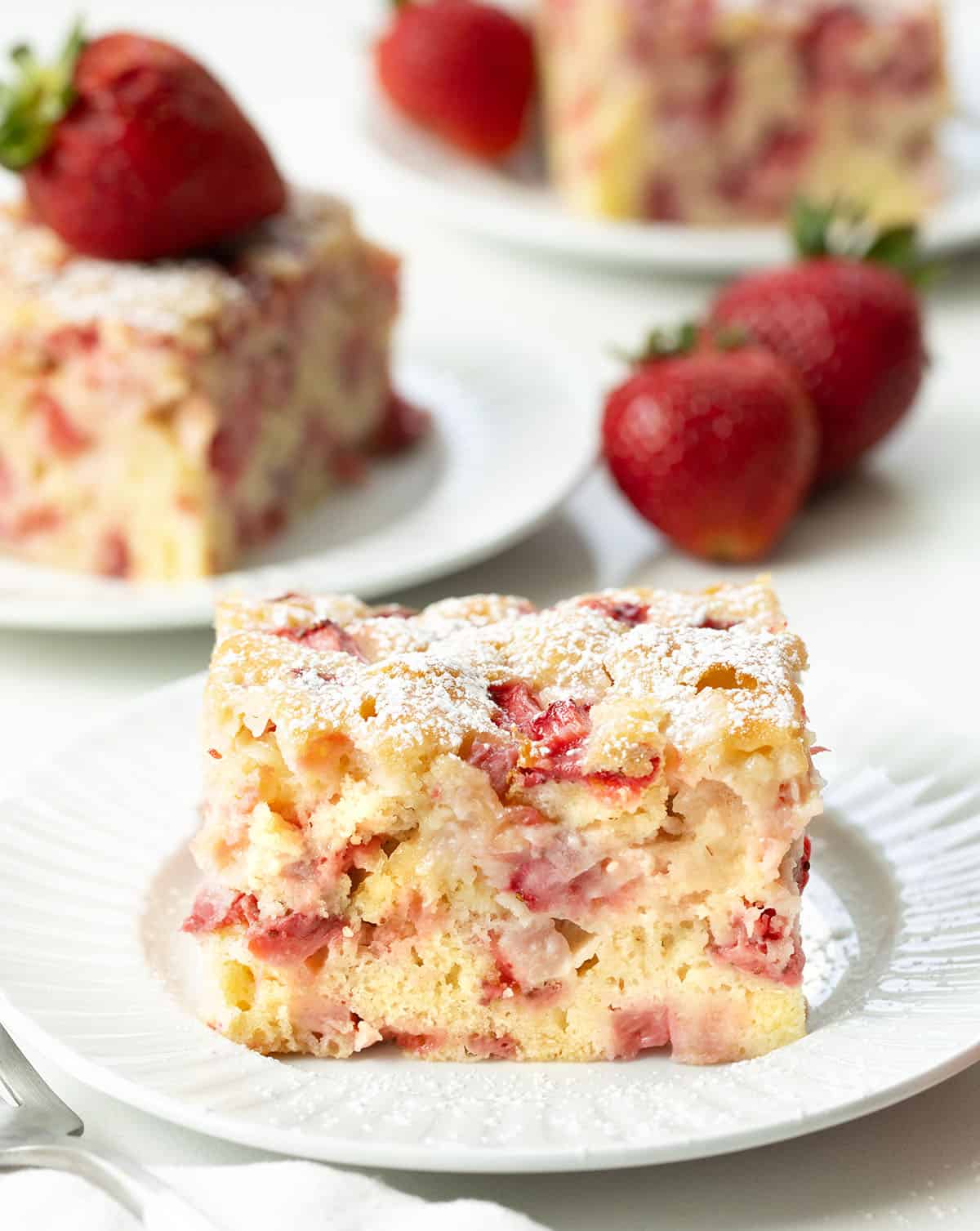 Slices of Old Fashioned Strawberry Sheet Cake on white plates on a white table.