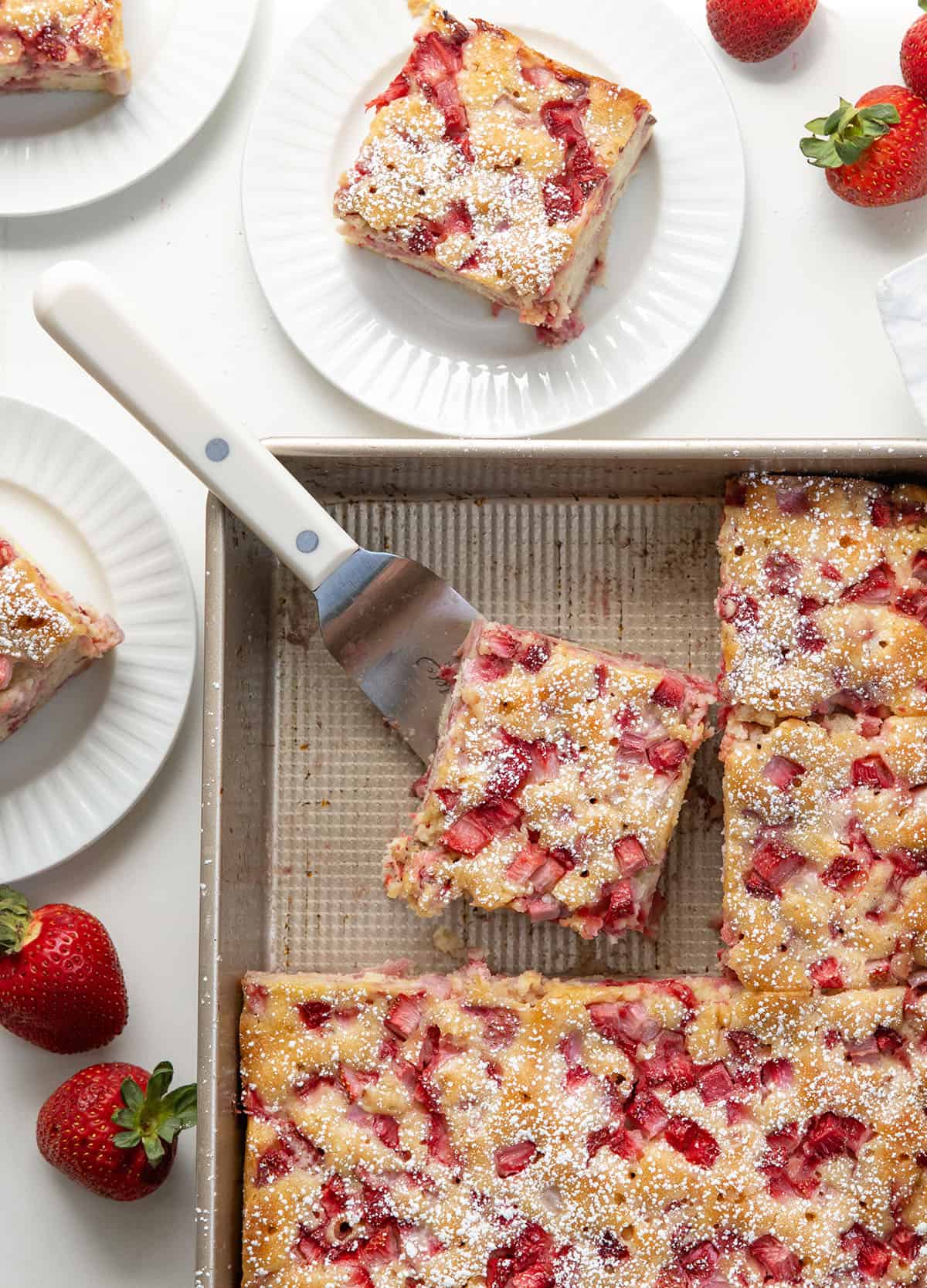 Old Fashioned Strawberry Sheet Cake cut in the pan and slices on white plates on a white table from overhead.