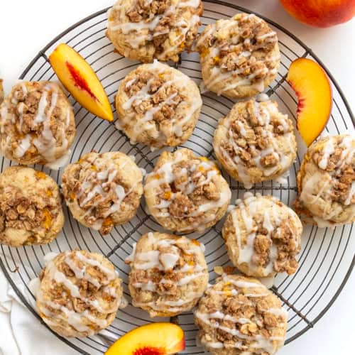 Wire rack filled with Peach Crisp Cookies and fresh peach on a white table from overhead.