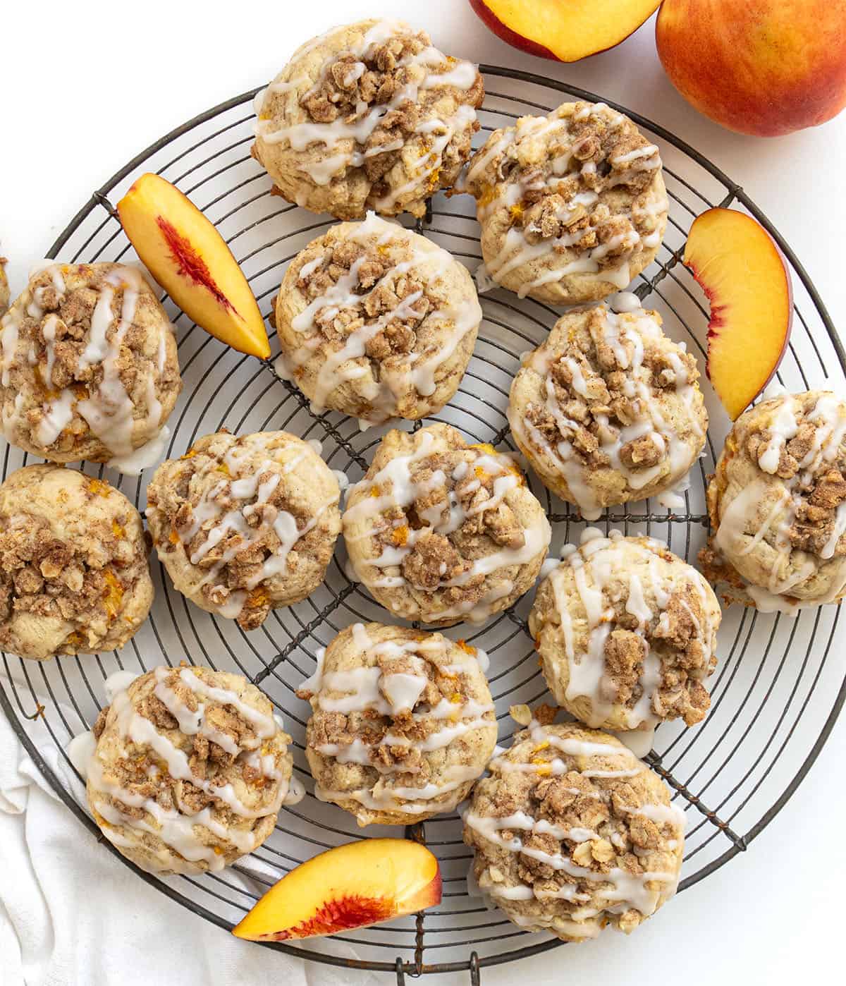 Wire rack filled with Peach Crisp Cookies and fresh peach on a white table from overhead.