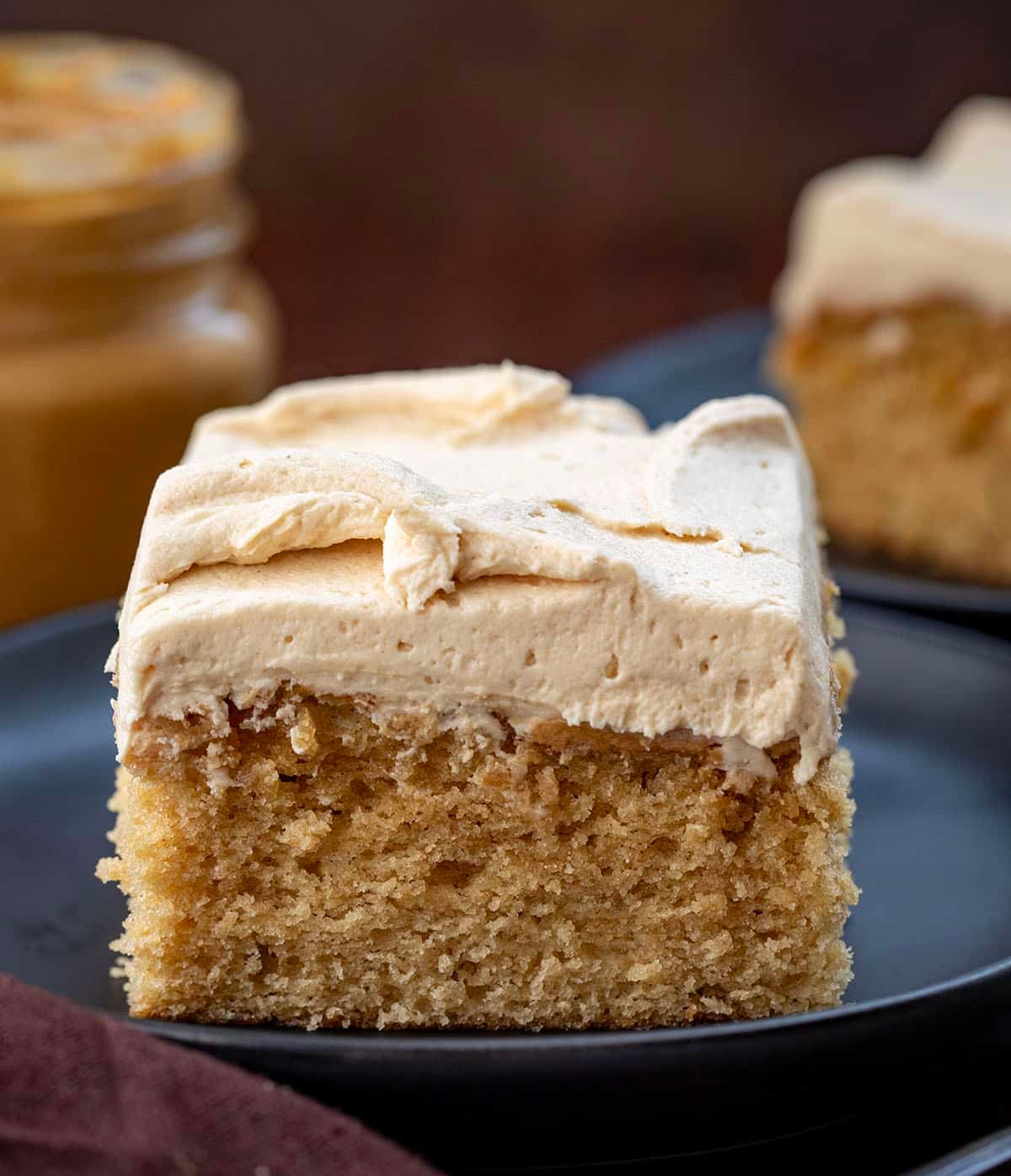 Slice of Peanut Butter Sheet Cake on a black plate with more cake and peanut butter in the background Slice of Peanut Butter Sheet Cake on a black plate with more cake and peanut butter in the background.
