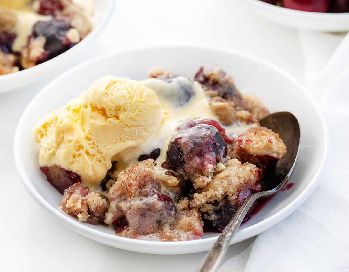 Bowls of Snickerdoodle Cherry Cobbler with vanilla ice cream on a white table.