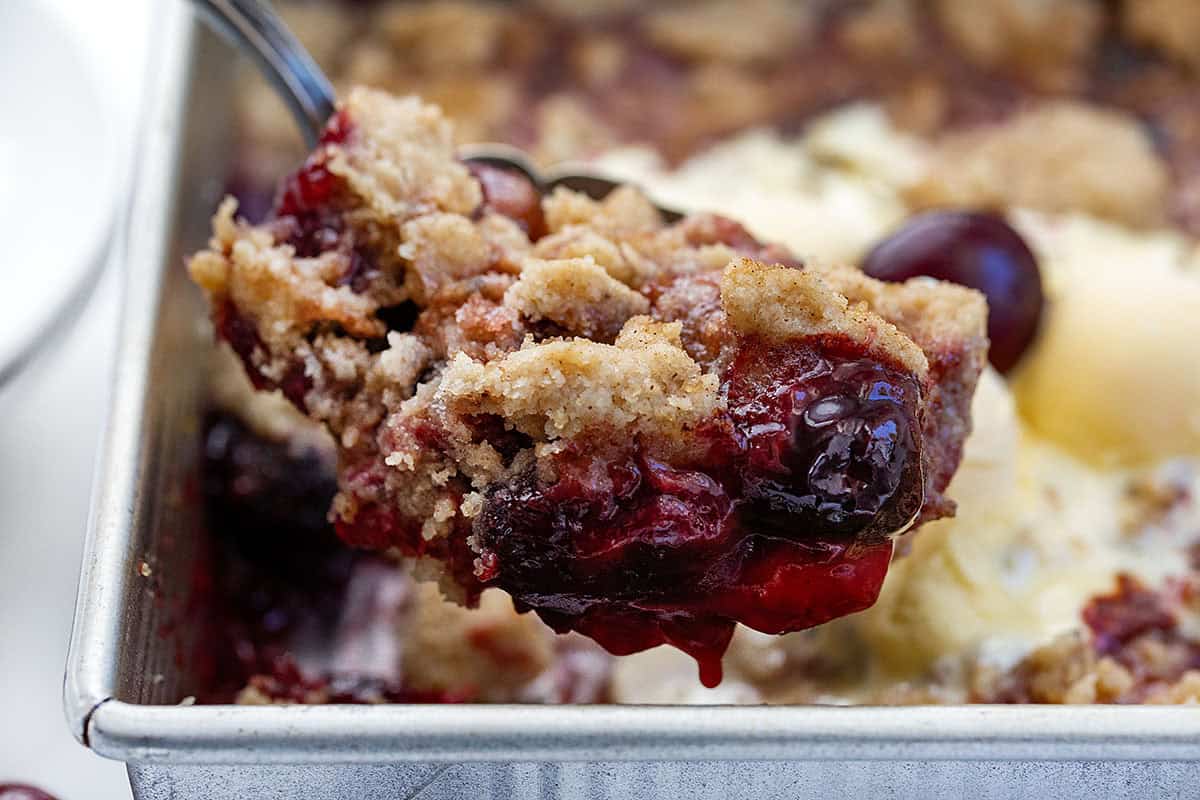 Close up of a scoop of Snickerdoodle Cherry Cobbler held above the pan.
