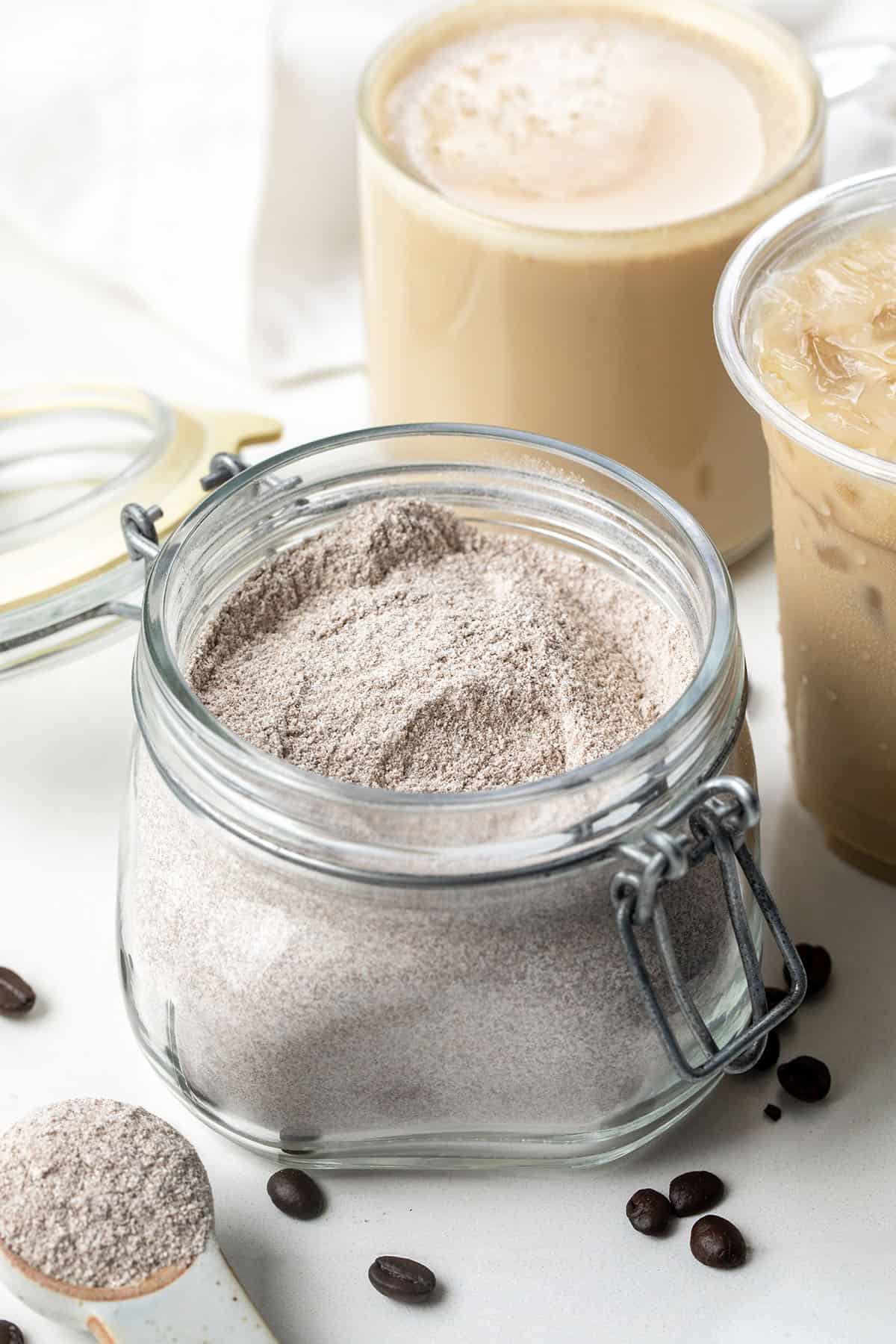 Jar of Vanilla Latte Mix on a white table with a hot vanilla latte and iced vanilla latte in the background Jar of Vanilla Latte Mix on a white table with a hot vanilla latte and iced vanilla latte in the background.
