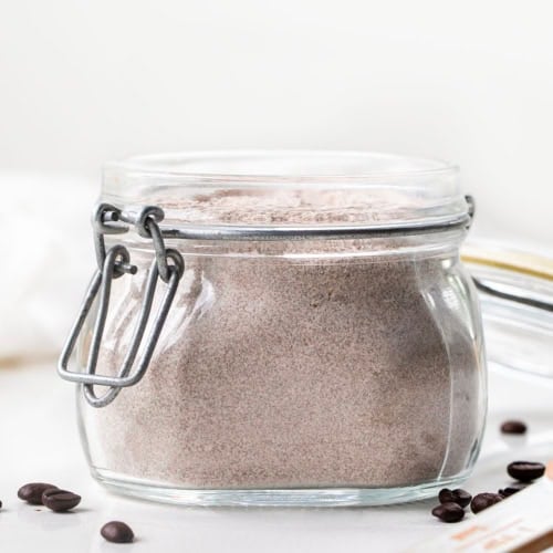 Glass jar of Vanilla Latte Mix on a white table with coffee beans.