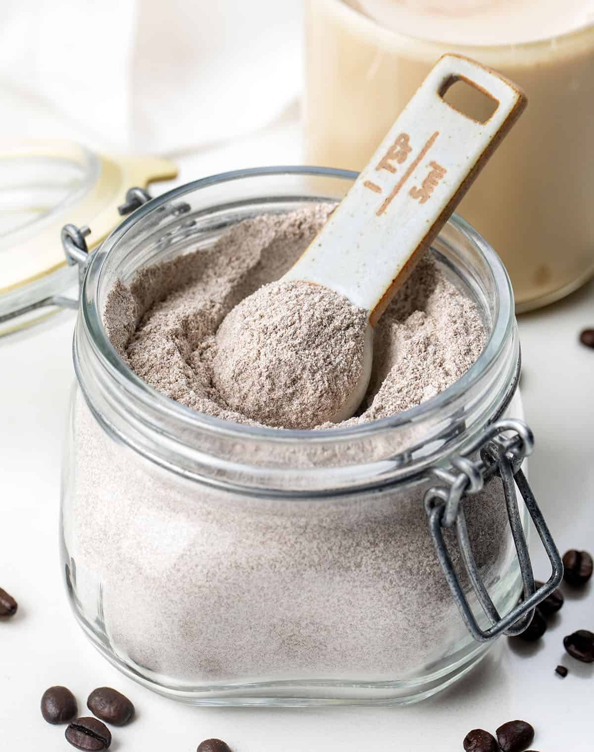 Close up of a jar of Vanilla Latte Mix in front of a hot vanilla latte.