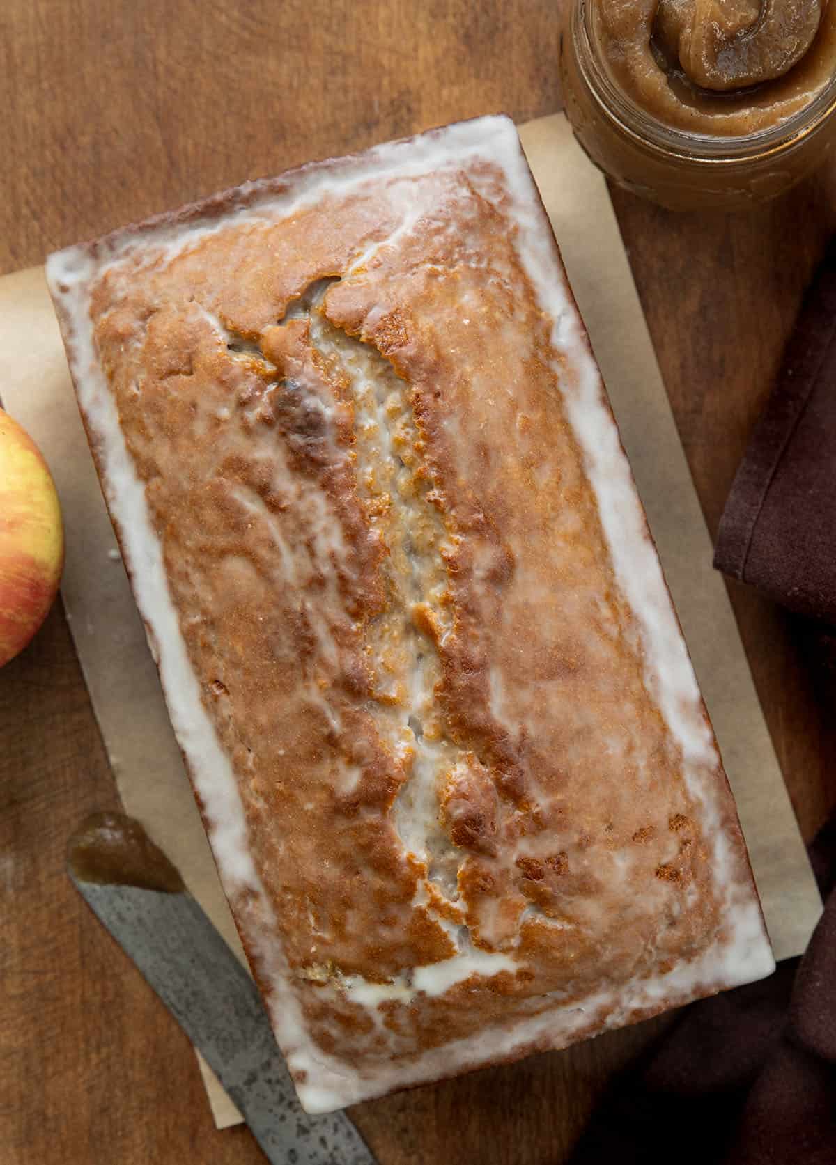 Glazed Apple Butter Bread on a wooden table with apple butter and an apple from overhead Glazed Apple Butter Bread on a wooden table with apple butter and an apple from overhead.