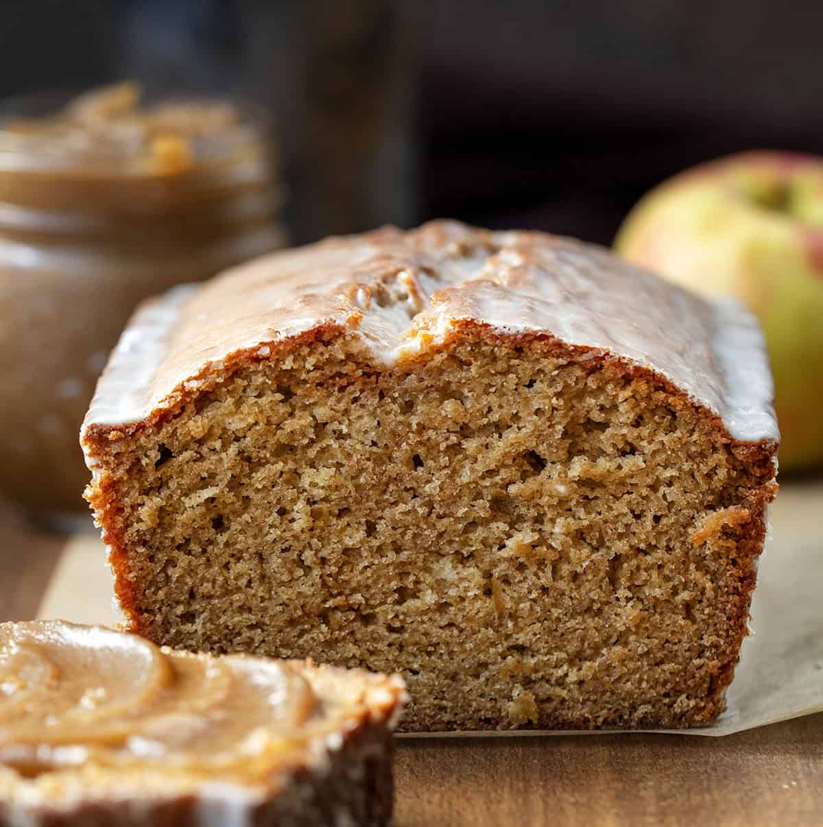Cut into loaf of Apple Butter Bread on a wooden table with apple butter and apples in the background Cut into loaf of Apple Butter Bread on a wooden table with apple butter and apples in the background.