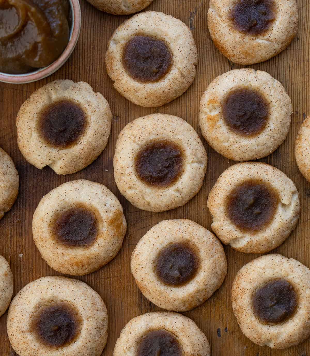 Apple Butter Thumbprint Cookies on a wooden table from overhead with a jar of apple butter next to them.