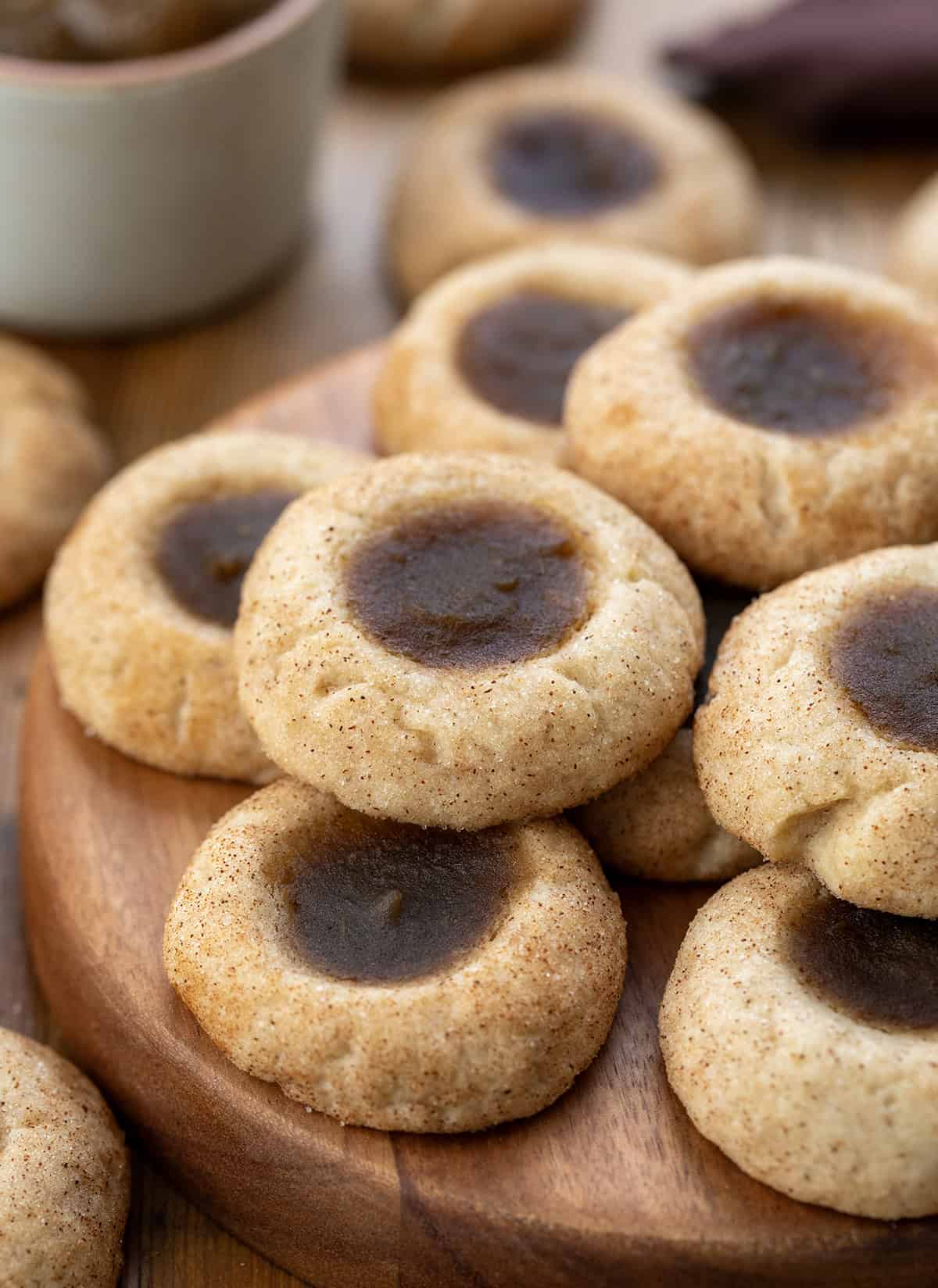Apple Butter Thumbprint Cookies on a plate on a wooden table surround by more cookies and apple butter.