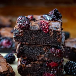 Stack of Blackberry Balsamic Brownies surrounded by more brownies on a wooden table.