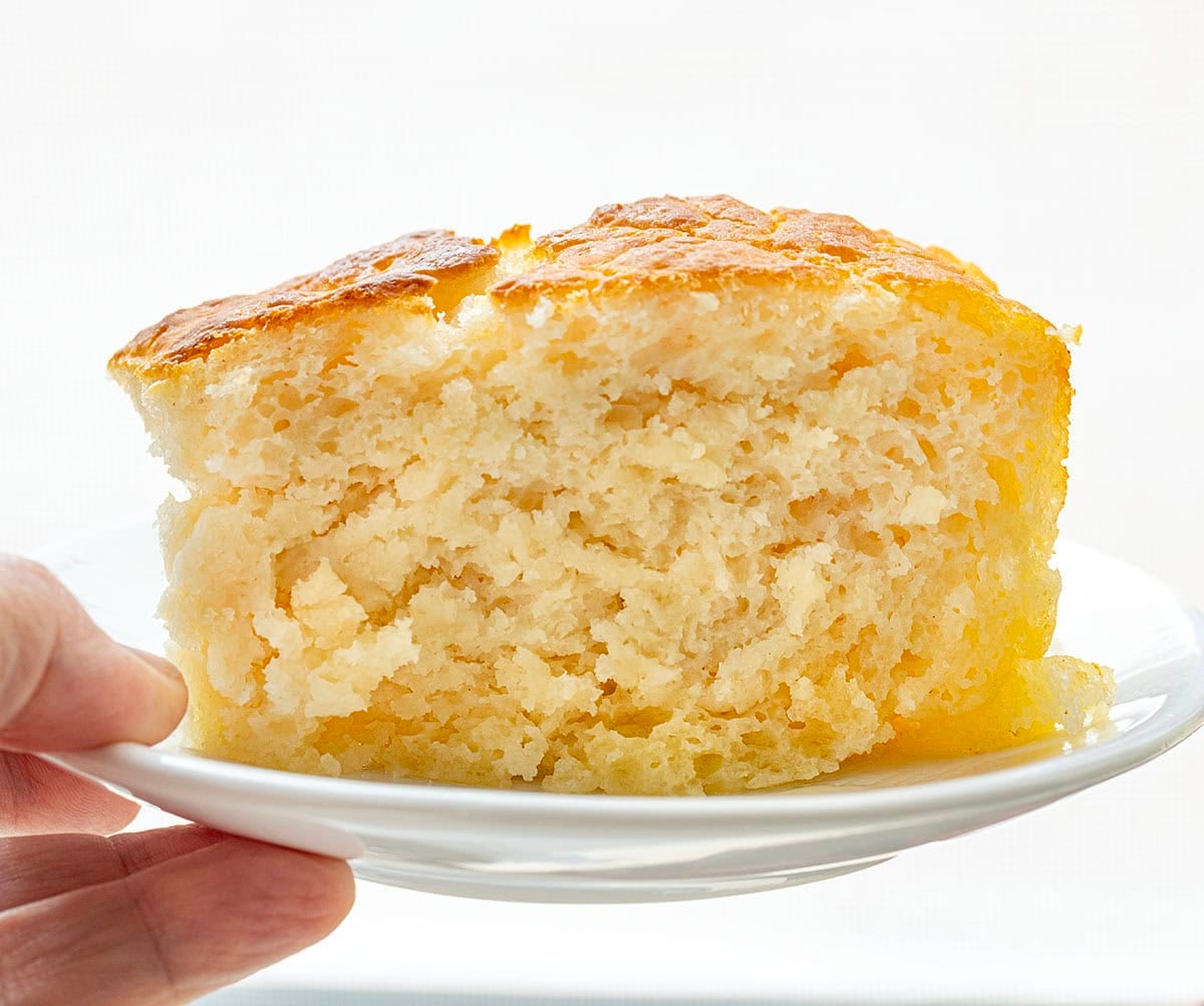 Close up of one butter swim biscuit on a white plate held by a hand.