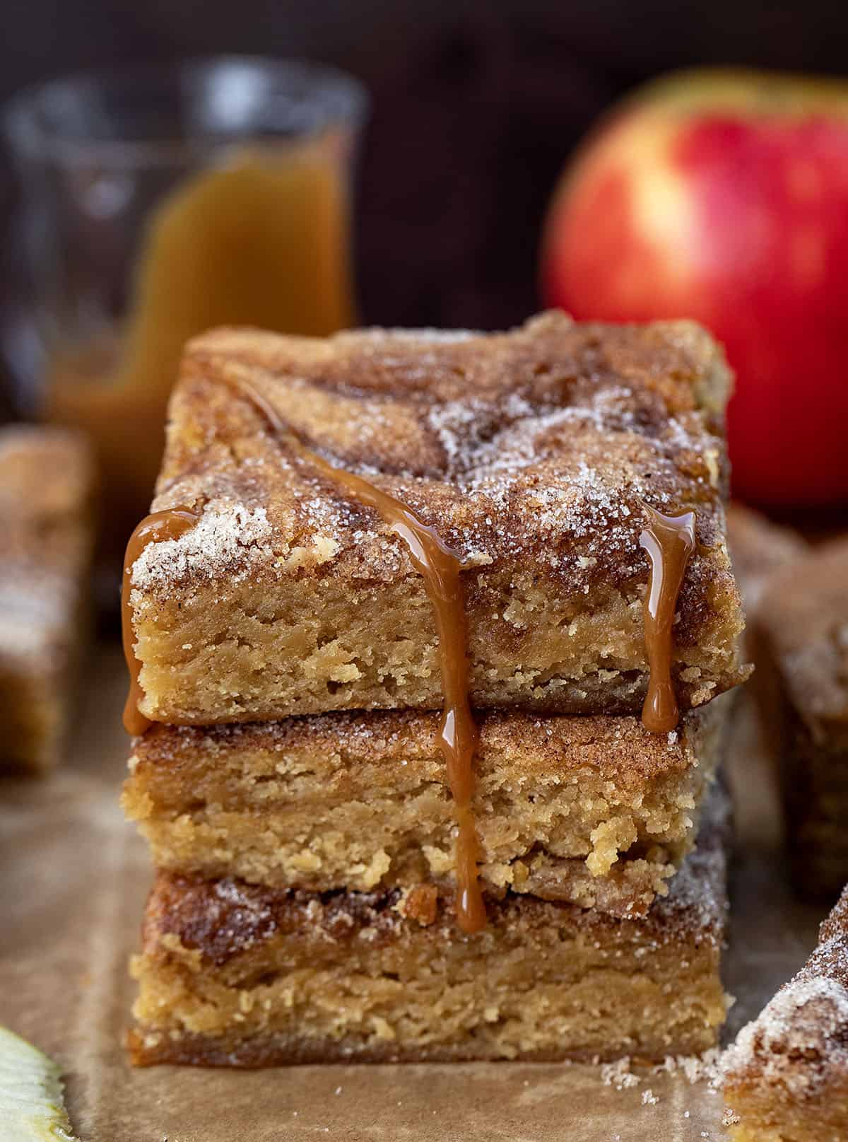 Stack of Caramel Apple Cider Blondies on a wooden table surrounded by caramel, apples, and more blondies Stack of Caramel Apple Cider Blondies on a wooden table surrounded by caramel, apples, and more blondies.