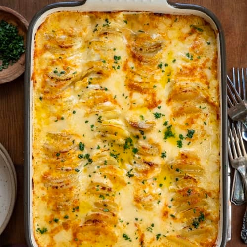 Cheesy Scalloped Potatoes in a large pan on a wooden table from overhead.