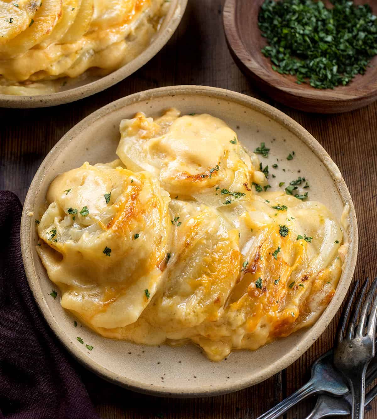 Plates of Cheesy Scalloped Potatoes on a wooden table.