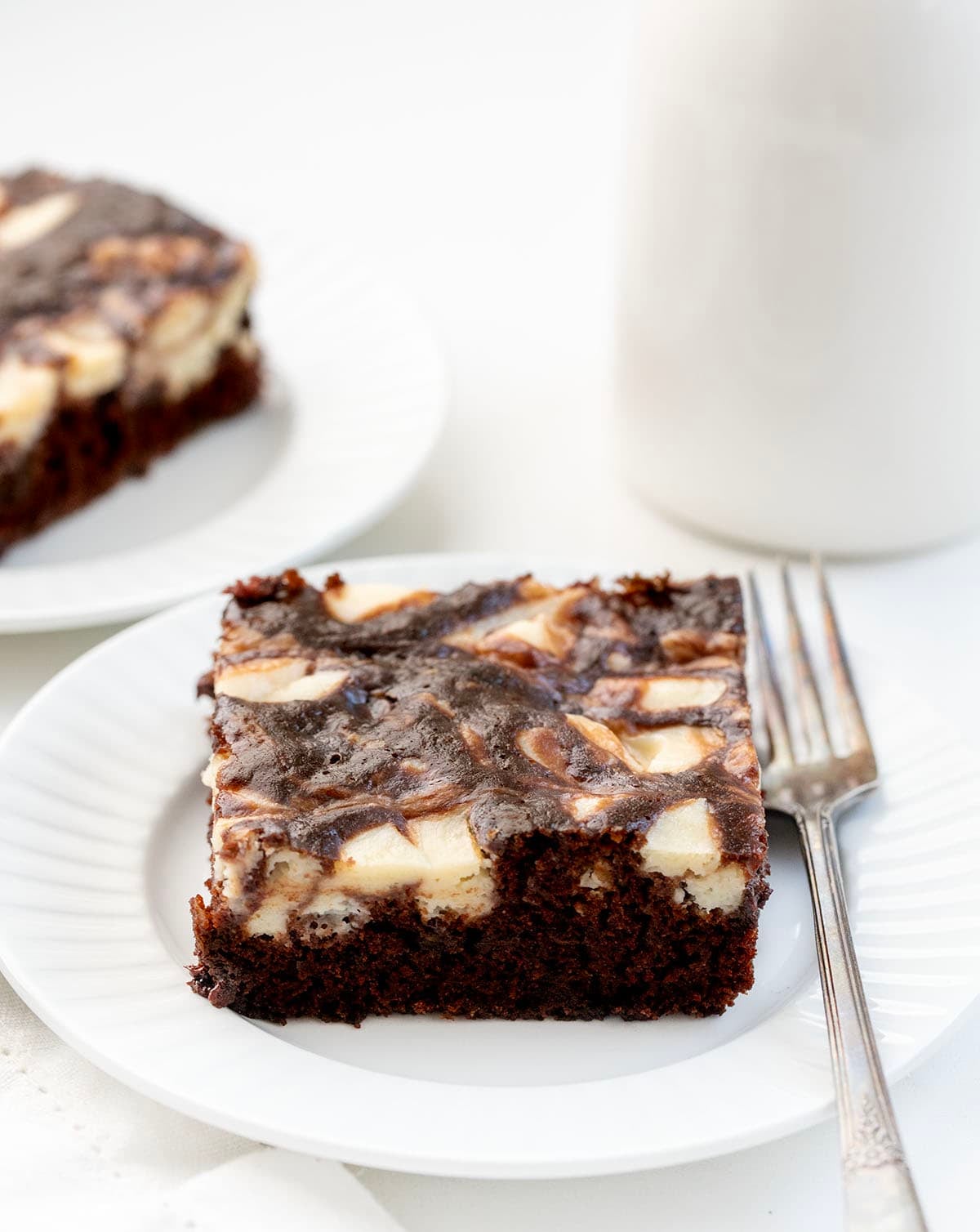 Pieces of Cream Cheese Chocolate Zucchini Cake on white plates on a white table.