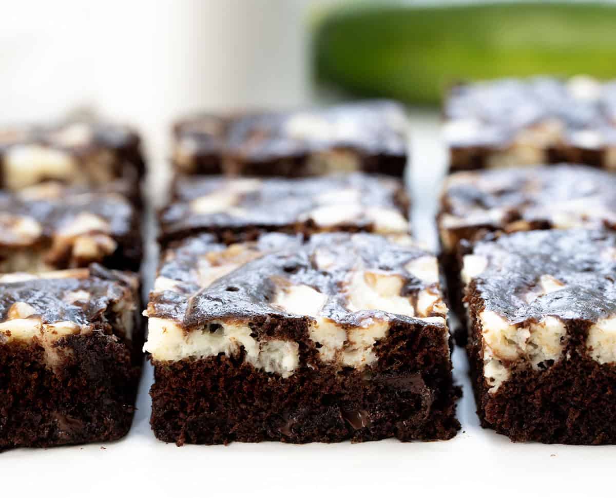 Close up of cut pieces of Cream Cheese Chocolate Zucchini Cake with zucchini in the background.