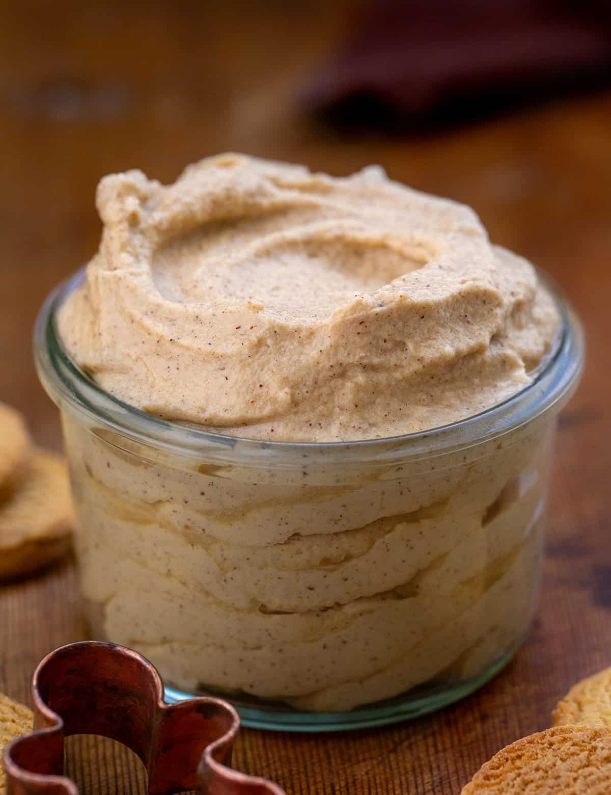 Jar of Gingerbread Stabilized Whipped Cream on a wooden table with ginger snap cookies.