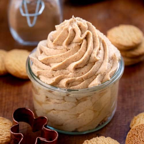 Gingerbread Stabilized Whipped Cream piped into a jar on a wooden table with homemade gingerbread spice in the background.