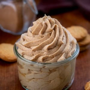 Gingerbread Stabilized Whipped Cream piped into a jar on a wooden table with homemade gingerbread spice in the background.