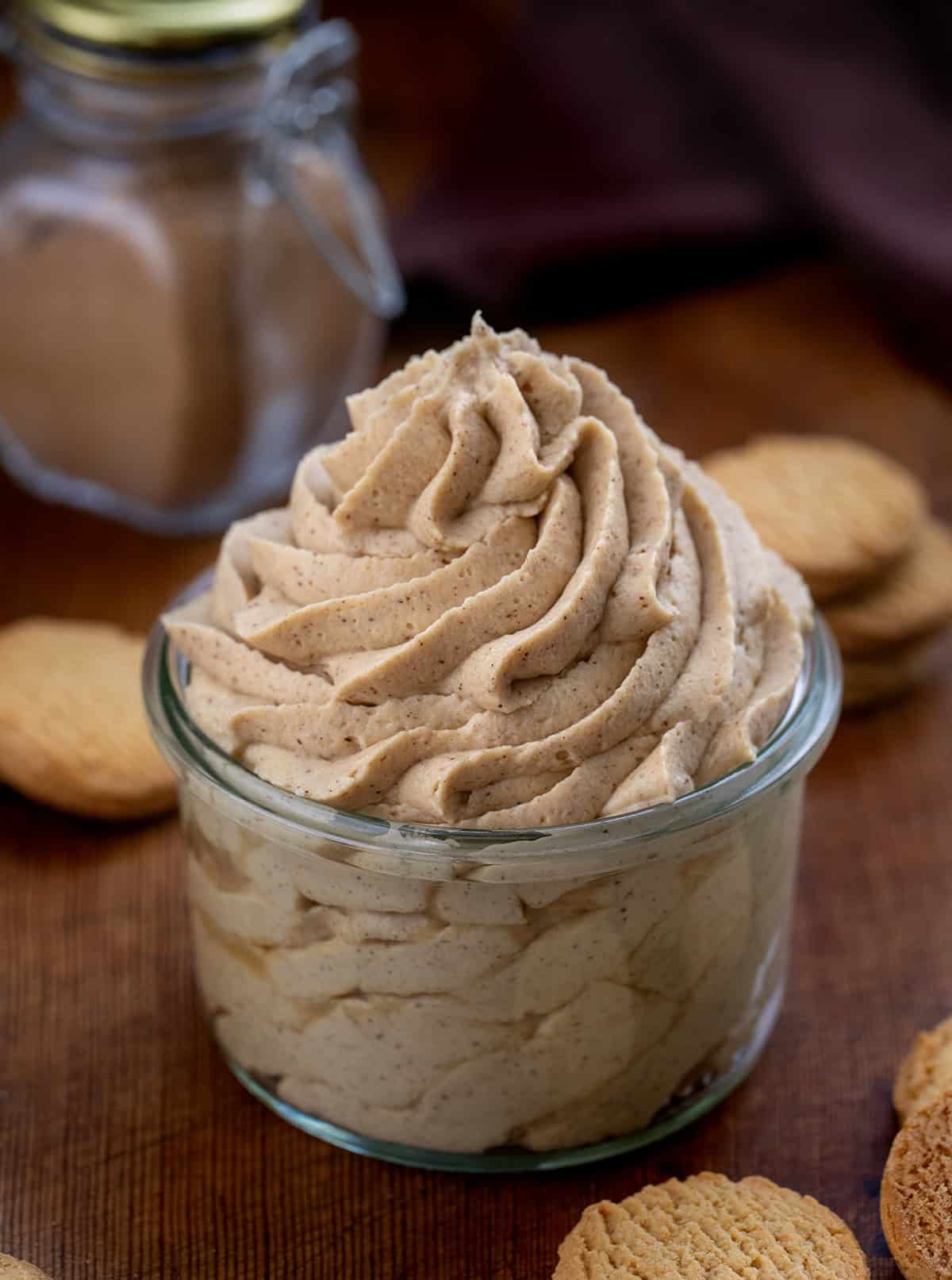 Gingerbread Stabilized Whipped Cream piped into a jar on a wooden table with homemade gingerbread spice in the background.