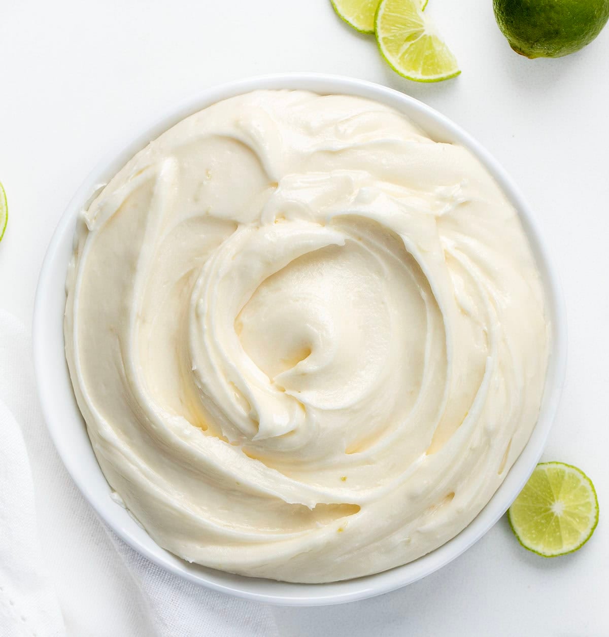 White bowl of Key Lime Marshmallow Buttercream on a white table with fresh lime.