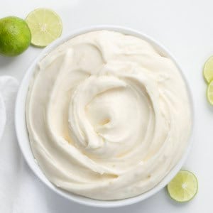 White bowl of Key Lime Marshmallow Buttercream on a white table with fresh lime.