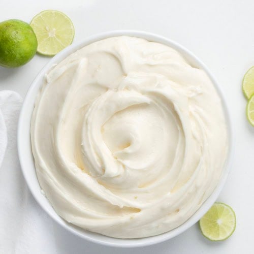 White bowl of Key Lime Marshmallow Buttercream on a white table with fresh lime.