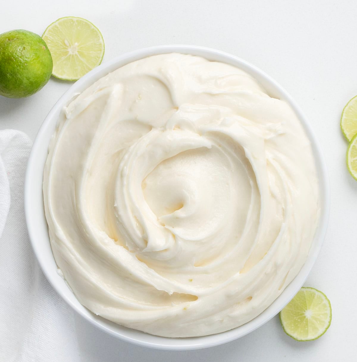 White bowl of Key Lime Marshmallow Buttercream on a white table with fresh lime.