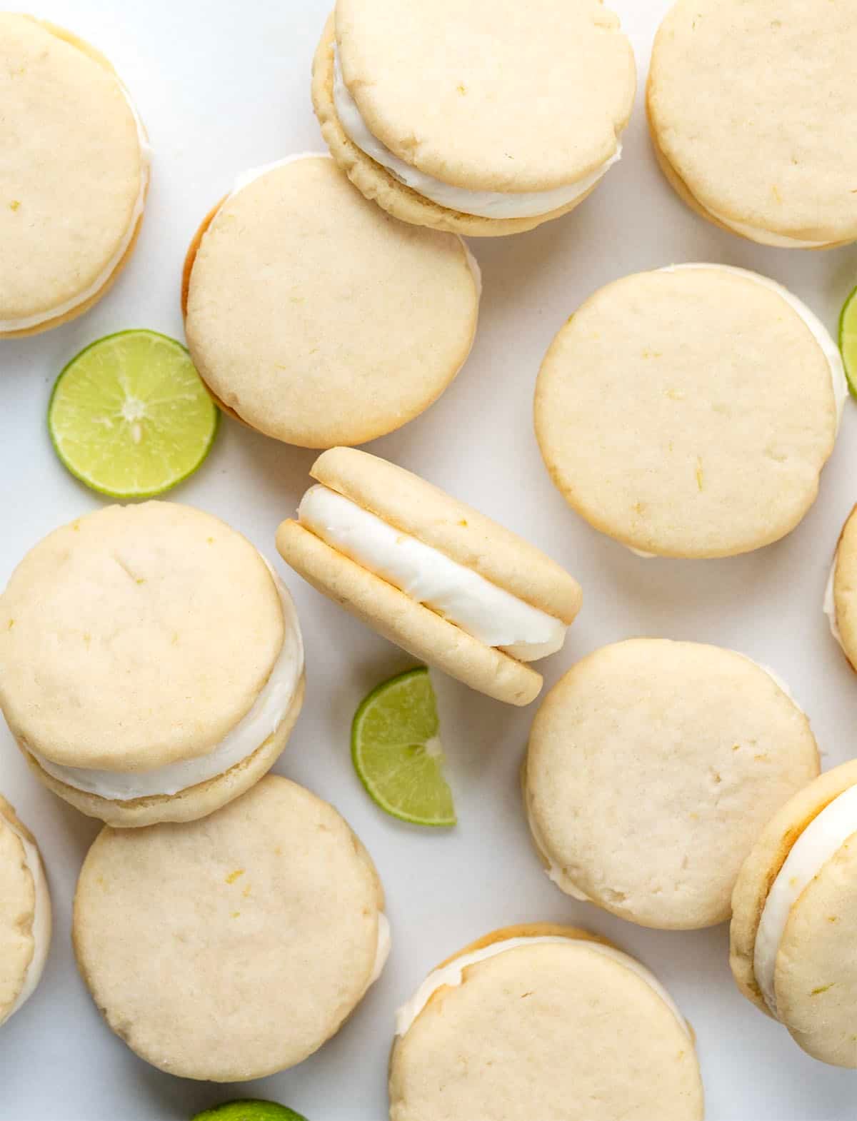 Key Lime Sandwich Cookies on a white table with fresh key lime from overhead. 