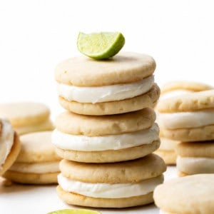 Stack of Key Lime Sandwich Cookies on a white table with a key lime wedge on top.
