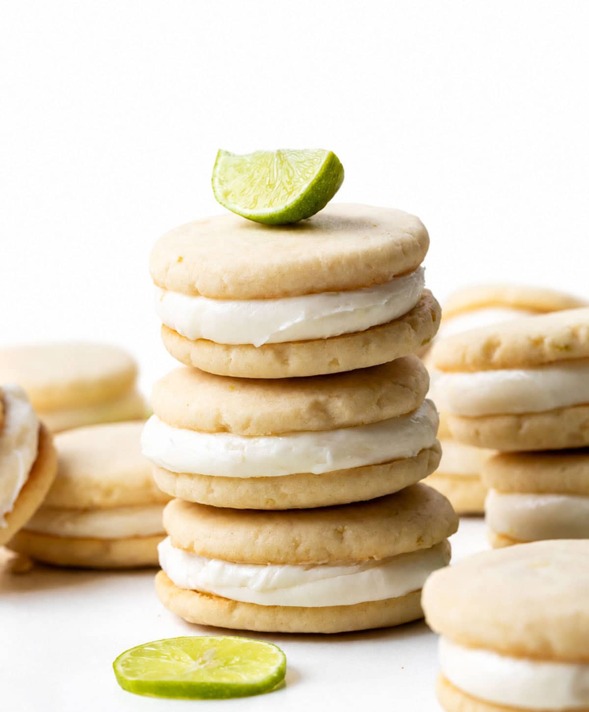 Stack of Key Lime Sandwich Cookies with Key Lime Marshmallow Buttercream on a white table with a key lime wedge on top.