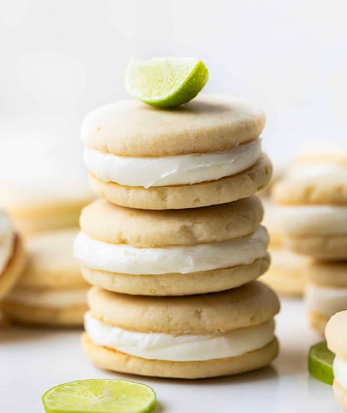Stack of Key Lime Sandwich Cookies on a white table with a key lime wedge on top.