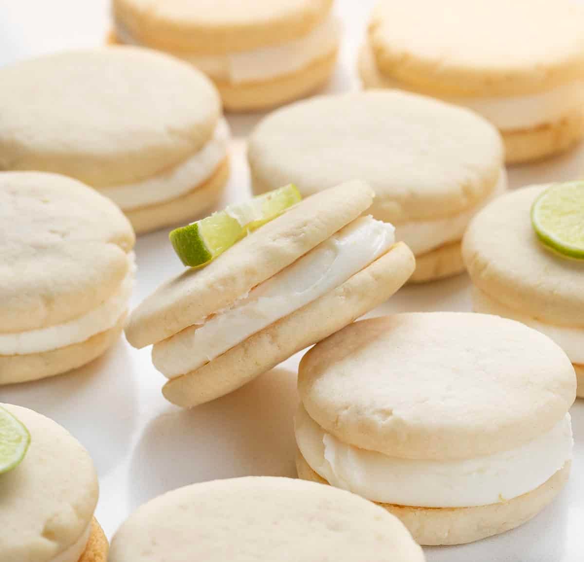 One Key Lime Sandwich Cookie on its side with the rest laying flat on a white table.