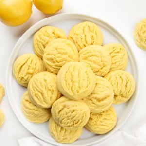 Lemon Sugar Cookies on a white plate on a white table with fresh lemons from overhead.