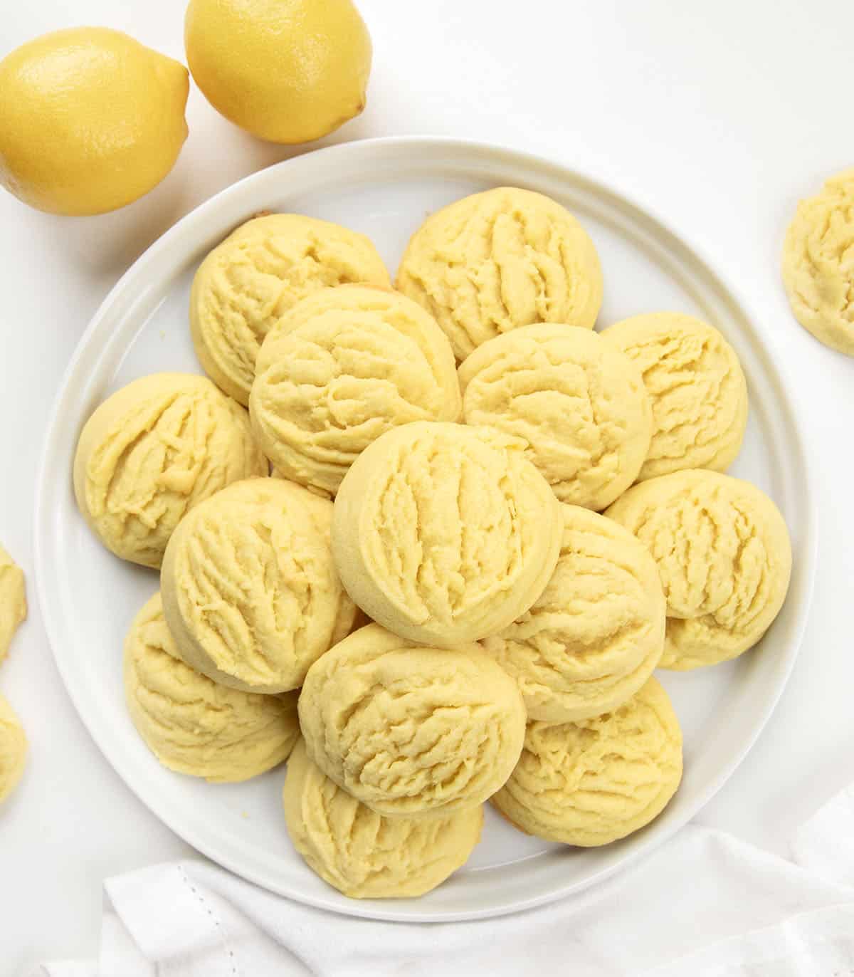 Lemon Sugar Cookies on a white plate on a white table with fresh lemons from overhead.