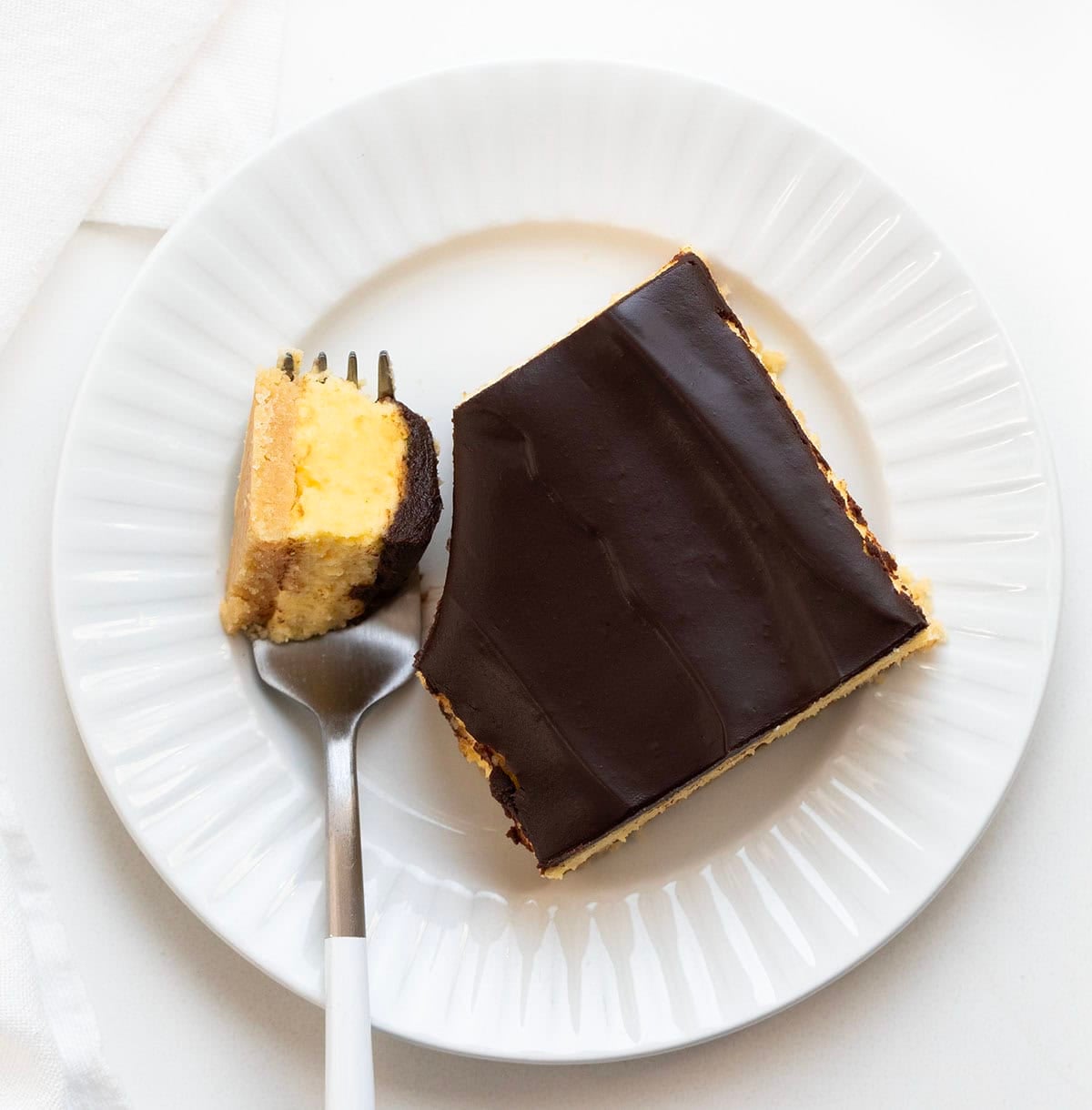 No Bake Boston Cream Pie Bar on a white plate with a small portion on a fork from overhead.