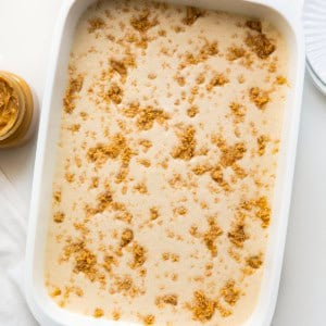 White pan with Peanut Butter Icebox Cheesecake in it on a white table with peanut butter from overhead.