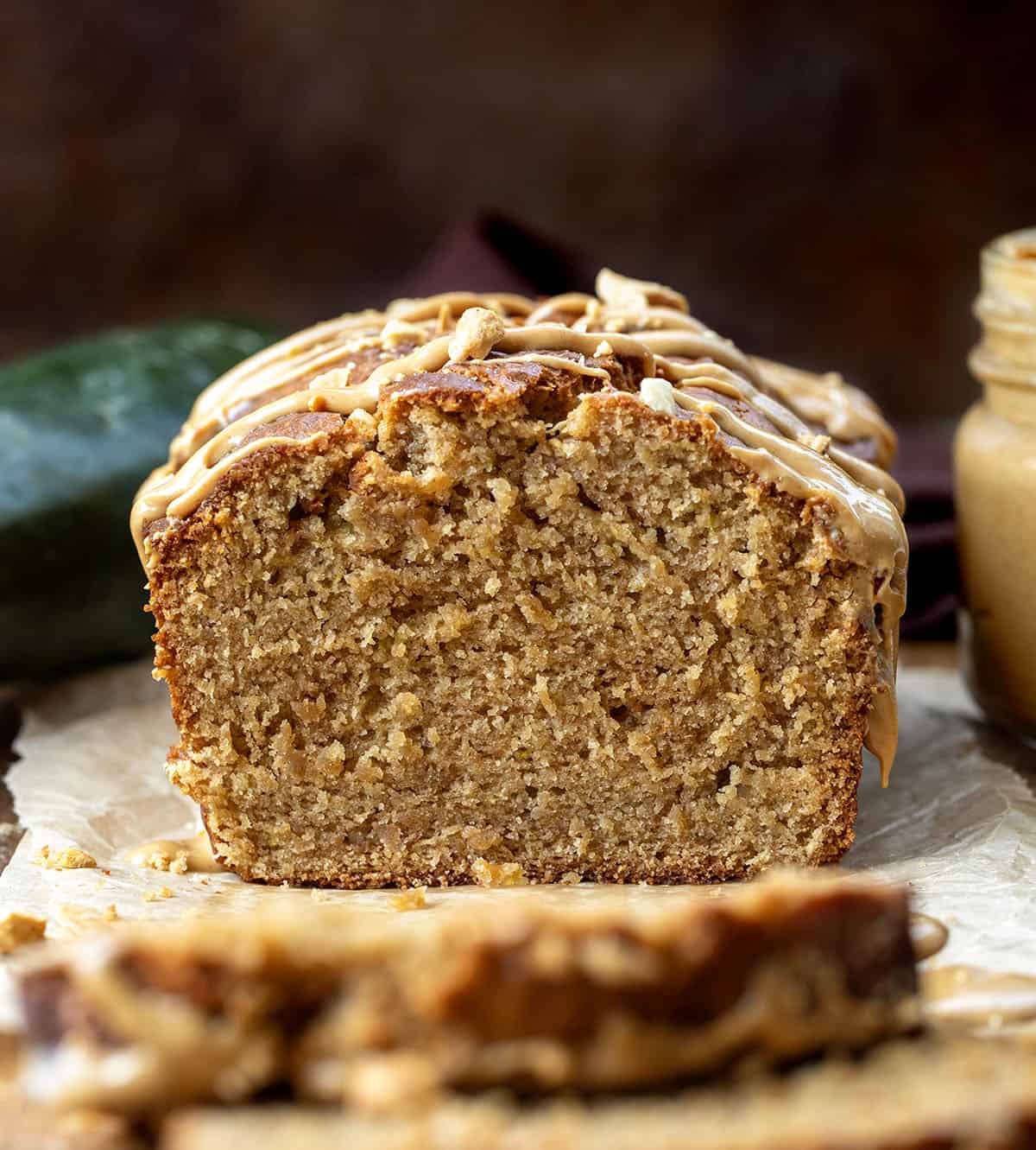 Close up of a cut into loaf of Peanut Butter Zucchini Bread near zucchini and peanut butter.